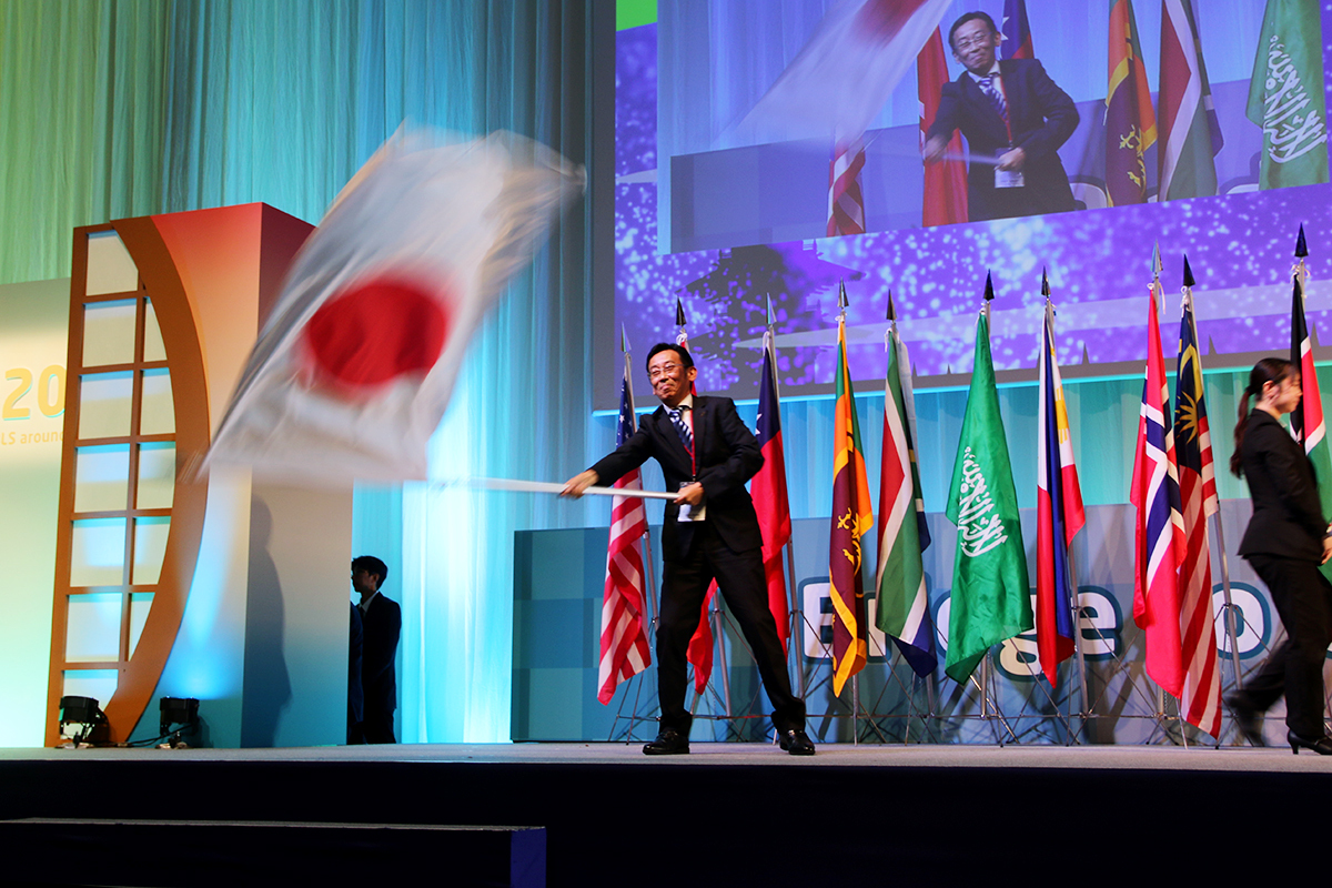ウェルカムセレモニーで国旗を掲げる丸田秀夫副会長